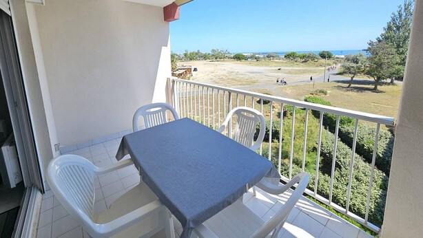 Ein Balkon mit Tisch und Stühlen, Blick auf einen Strand und einen klaren Himmel.