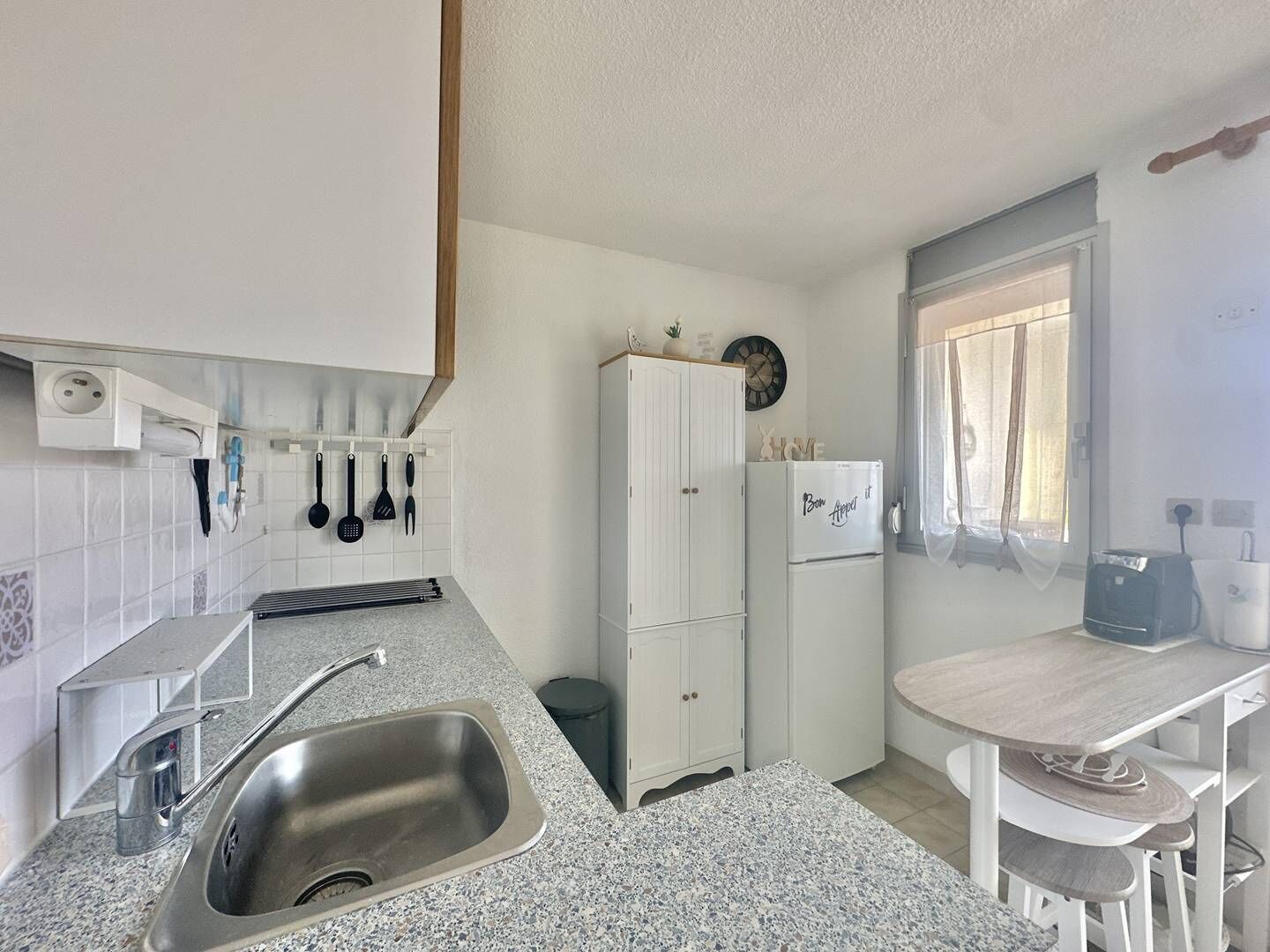 A compact kitchen with a sink, cabinets, a countertop, and a window.