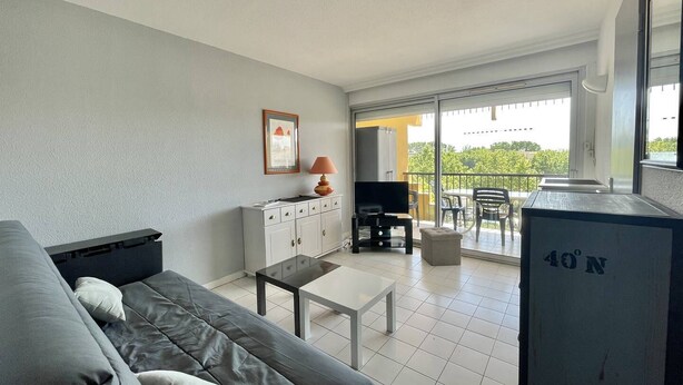 A modern living room with a sofa, a TV, a small table, and a balcony with outdoor furniture. - CAP D'AGDE - Plage Richelieu / Réf 193 (CAP D'AGDE)