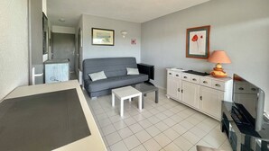 A compact living space with a grey sofa, a small white table, a cabinet with drawers, and a television. - CAP D'AGDE - Plage Richelieu / Réf 193 (CAP D'AGDE)