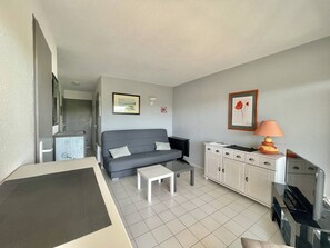 A compact living space with a grey sofa, a small white table, a cabinet with drawers, and a television. - CAP D'AGDE - Plage Richelieu / Réf 193 (CAP D'AGDE)