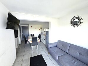 A modern living room with a grey sofa, a dining area with chairs and a table, and a kitchen with a refrigerator. - CAP D'AGDE - Plage du Môle / Réf 236 (CAP D'AGDE)