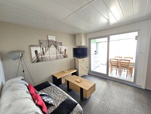 Una sala de estar moderna con un sofá, una mesa de centro, un televisor y un ventanal corredero que da a un patio exterior.