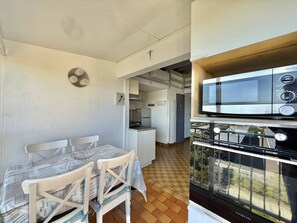 A compact kitchen with a microwave, oven, and a dining area with a table and chairs. - CAP D'AGDE - Plage du Môle // Réf 0105 (CAP D'AGDE)
