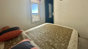 Une chambre à coucher avec un lit, une fenêtre donnant sur un beau paysage, une porte et un petit tableau accroché au mur.