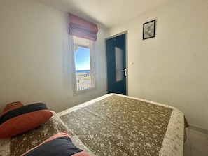 Ein Schlafzimmer mit Bett, Fenster mit Blick, einer Tür und einem kleinen Bild an der Wand.