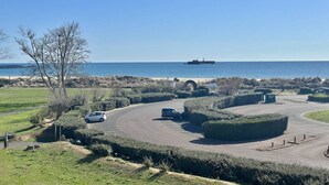 Un espace de stationnement avec une route sinueuse, un arbre et une vue lointaine sur la mer.