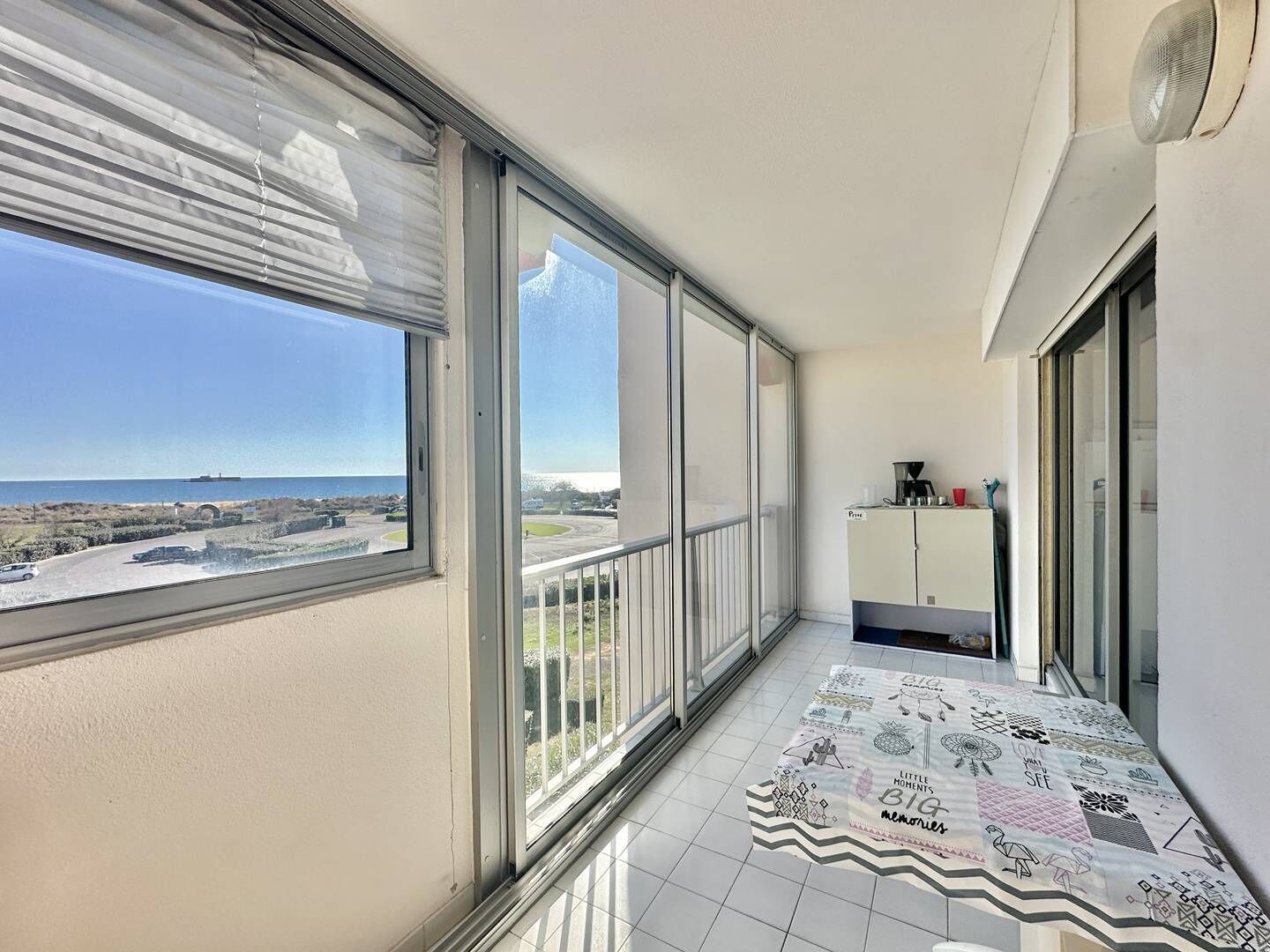 A balcony with large windows, a tiled floor, and a view of the sea and a ship.
