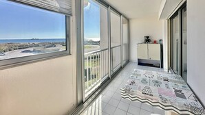 Un balcon doté de grandes fenêtres, d’un sol carrelé et offrant une vue sur la mer et un navire.