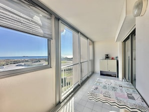 Ein Balkon mit großen Fenstern, Fliesenboden und Blick auf das Meer und ein Schiff.
