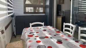 Habitación pequeña con mesa de comedor, sillas, ventana con persianas, televisión y un mueble bajo.