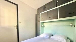 Una cama individual con ropa blanca, un cabecero verde claro y un conjunto de armarios grises arriba.