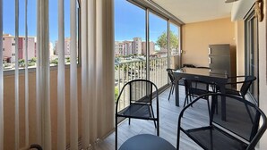 Een balkon met een tafel en stoelen, grote ramen en uitzicht op gebouwen.