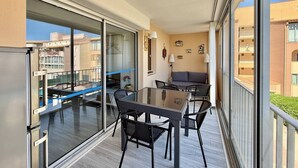 Een balkon met een glazen deur, een eettafel met stoelen, een bank en een bijzettafeltje met een lamp.