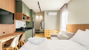 Una habitación de hotel con cama, escritorio, silla, kitchenette y televisor.