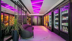 Un moderno vestíbulo de hotel con una zona de estar curva, una planta grande en maceta y dispensadores de bebidas refrigeradas a lo largo de las paredes.
