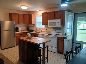 A kitchen with wooden cabinets, a stainless steel refrigerator, a microwave, a stove, and a dining area with a table and chairs.