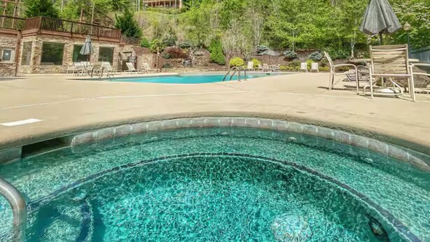 Piscina límpida com espreguiçadeiras e guarda-sóis, cercada por árvores e um edifício de pedra.