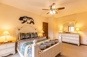 A bedroom with a bed, nightstands, a dresser, a ceiling fan, a mirror, and a bear wall decoration.