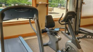 Uma academia com equipamentos de cardio, um banco de musculação e vista para o exterior.