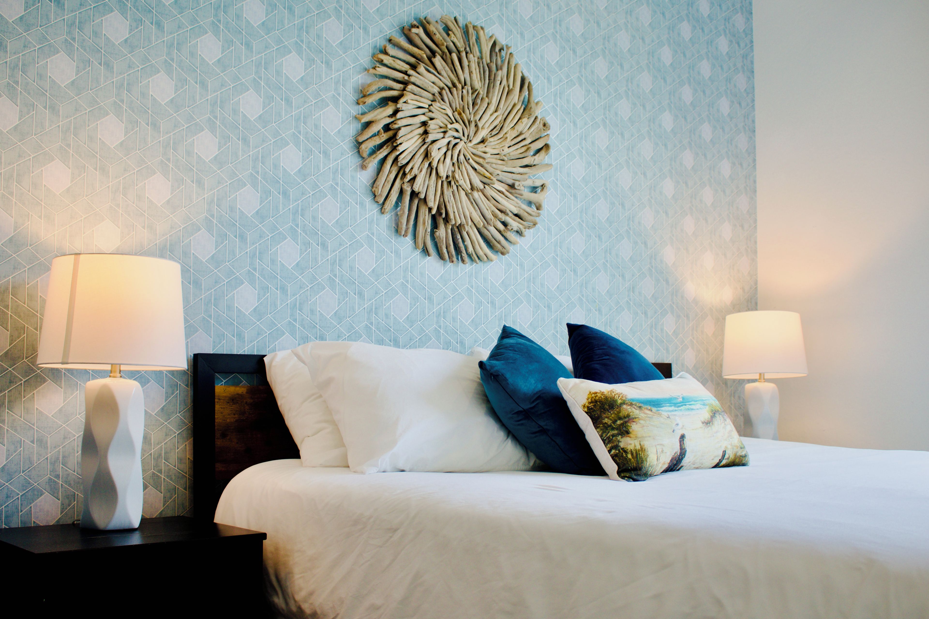 A hotel room with a bed, two bedside lamps, a decorative wall piece, and a geometric patterned wall.