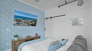 Een slaapkamer met een bed, nachtkastje, wandtelevisie, raam en deur.