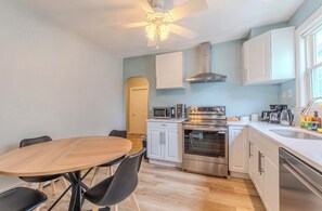 A compact kitchen with a dining area, white cabinets, a microwave, an oven, and a ceiling fan.
