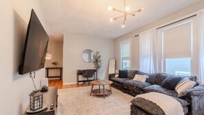 Un salon moderne avec un téléviseur à écran plat, un canapé, une table basse et un lustre.