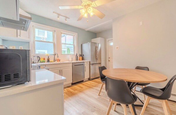 A compact kitchen with a dining area, a ceiling fan, and a refrigerator.