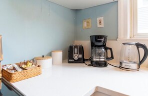A kitchen with a coffee maker, a glass carafe, a toaster, and a wicker basket with items.
