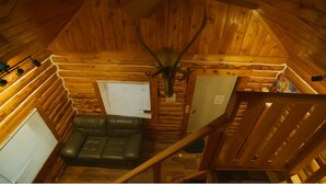 A log cabin interior with a leather sofa, a ceiling fan, wooden walls, and a staircase. - Alaska Homestead Roadhouse (Delta Junction)