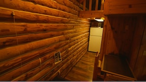 A log cabin interior with wooden walls, a white refrigerator, and a wooden cabinet. - Alaska Homestead Roadhouse (Delta Junction)
