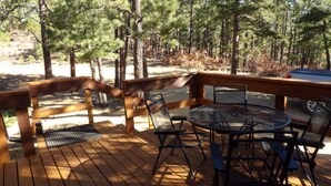 Una terraza de madera con una mesa y sillas, rodeada de árboles.