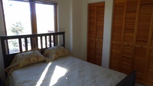 Un dormitorio con cama, ventana y un juego de armarios de madera.