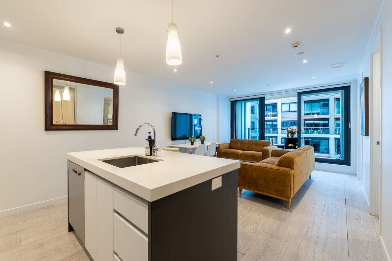 A modern kitchen with a central island, a dining area with a sofa, and large windows offering a city view.