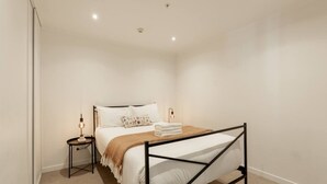 Een slaapkamer met een bed, nachtkastje, lamp en een wandlamp.