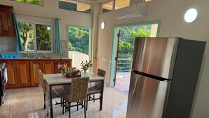 A kitchen with a dining table, chairs, a refrigerator, and a view of greenery outside. - Tranquil & private 1-bedroom fully furnished AC apartment in charming Soufrière (Soufrière)
