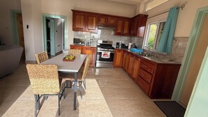 A modern kitchen with wooden cabinets, a dining table with chairs, and a built-in oven. - Tranquil & private 1-bedroom fully furnished AC apartment in charming Soufrière (Soufrière)