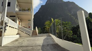 A building with a staircase leading to a balcony, surrounded by a chain-link fence and lush greenery. - Tranquil & private 1-bedroom fully furnished AC apartment in charming Soufrière (Soufrière)