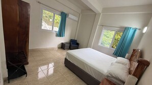A bedroom with a bed, a wooden wardrobe, a small table, a chair, and two windows with curtains. - Tranquil & private 1-bedroom fully furnished AC apartment in charming Soufrière (Soufrière)