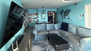 A living room with a sectional sofa, a small table, a bookshelf, and a world map on the wall.