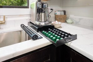 Eine Küche mit einer Kaffeemaschine, einer Schublade voller grüner Flaschen und einem Korbkörbchen mit Schüsseln.