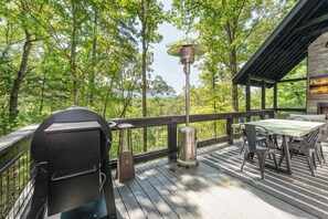 An outdoor deck with a grill, a table with chairs, and a view of a forested area. - Luxe A-frame Hideaway, mountain views, hot tub, outdoor patio w/fireplace (Blairsville)