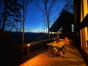 A wooden deck with a table and chairs, overlooking a mountainous landscape. - Luxe A-frame Hideaway, mountain views, hot tub, outdoor patio w/fireplace (Blairsville)