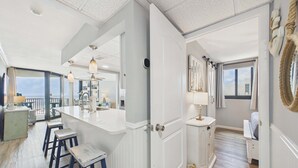 Une cuisine spacieuse avec un grand îlot central, un coin repas avec des tabourets de bar, une vue sur l’océan et un salon agrémenté d’une grande fenêtre.