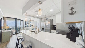Une cuisine moderne dotée d’un grand îlot central, d’appareils électroménagers en acier inoxydable et offrant une vue sur l’extérieur.