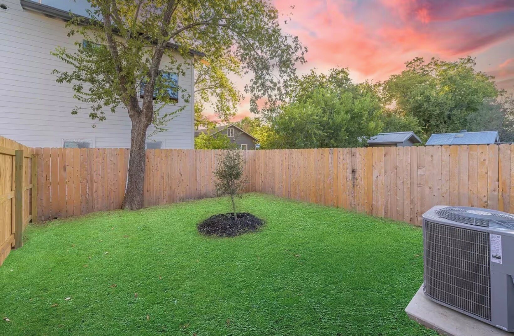 A backyard with a wooden fence, a small tree, and an air conditioning unit.