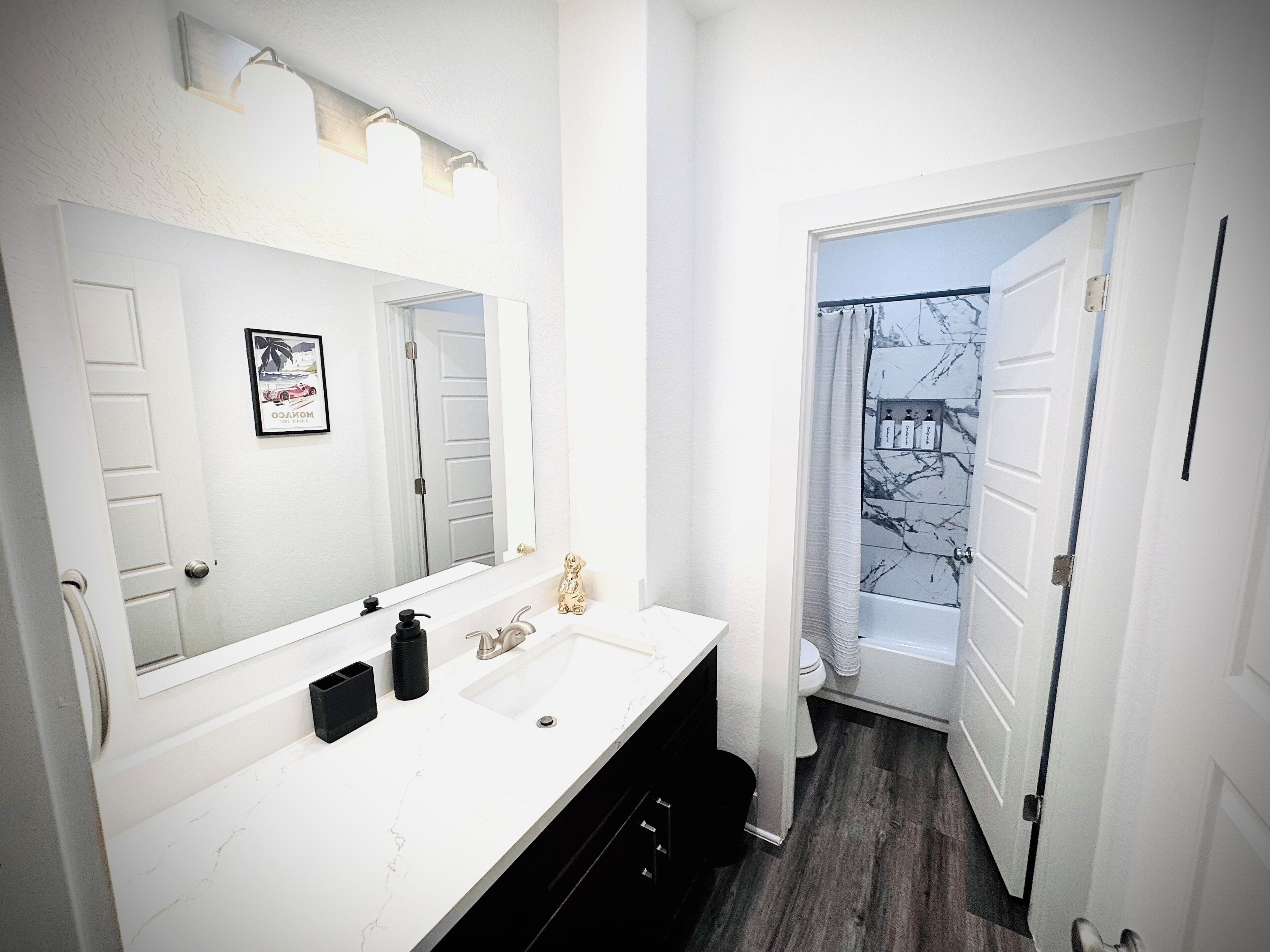 A bathroom with a white vanity, a large mirror, a framed picture, and a shower with a marble wall.