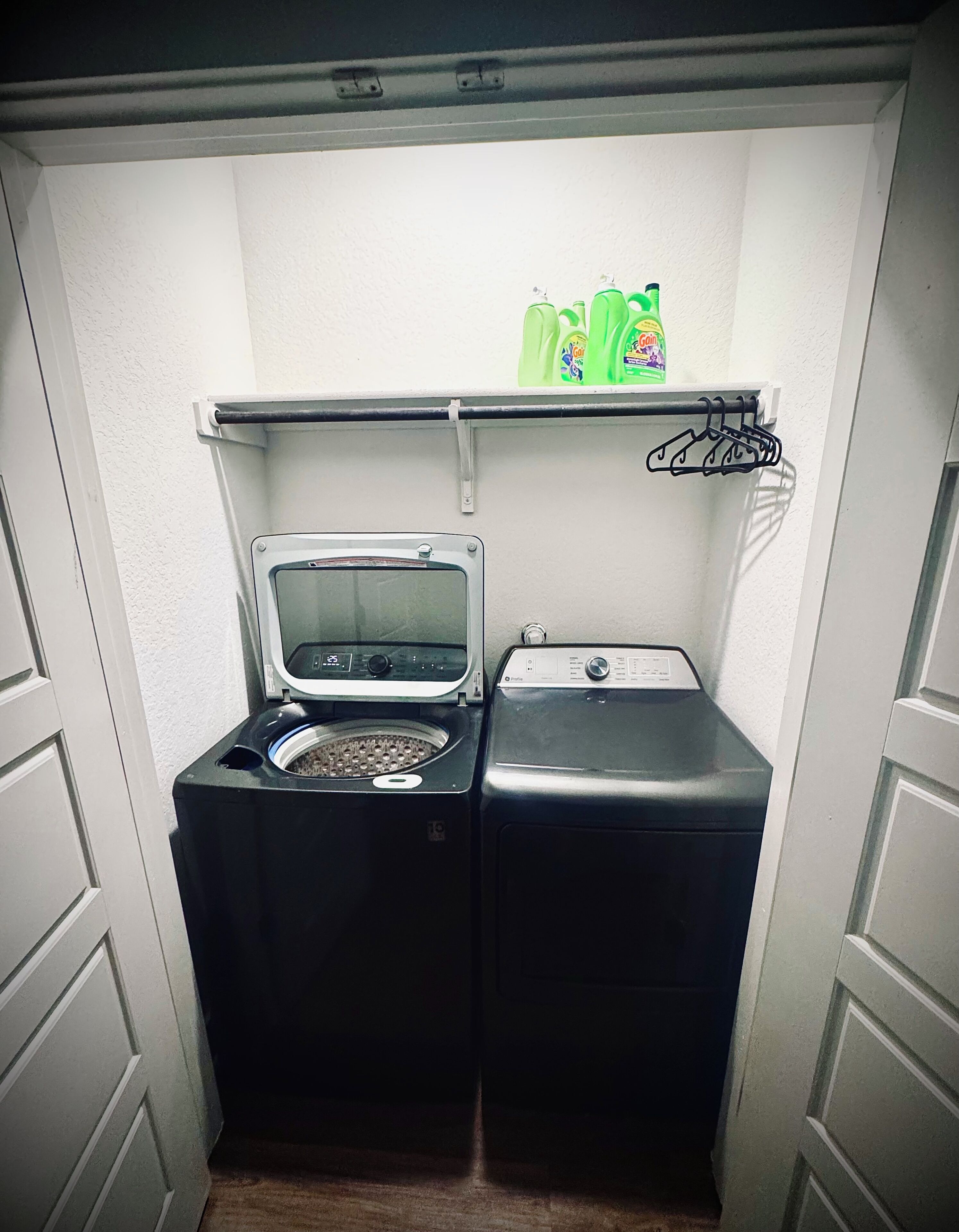 Un espace buanderie compact comprenant un lave-linge et un sèche-linge, une étagère avec des bouteilles de lessive et un étendoir.