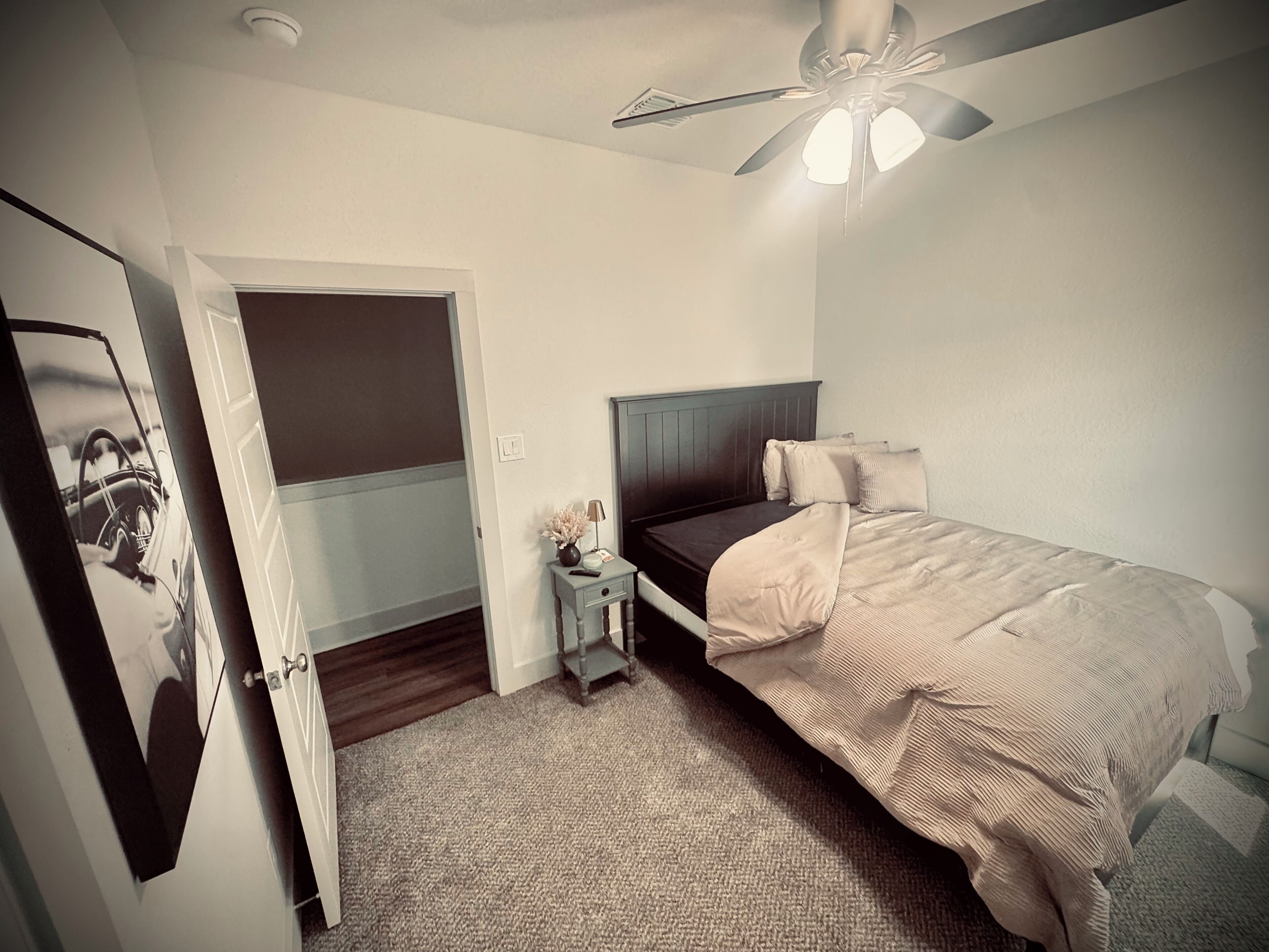 Un dormitorio con cama, mesita de noche, ventilador de techo y una puerta.
